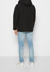 Svart isolerad jacka med huva, med en slät yta. Kombineras med ljusblå jeans och vita sneakers.