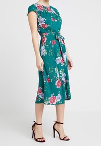 Květinové midi šaty v teal barvě se zkrácenými rukávy, detaily pásku a živými růžovými a fialovými květy. Hladká tkanina a áčkový střih.