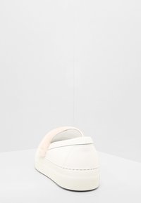 Biały tenisówka z konstrukcją wsuwaną, ozdobiona puszystym różowym akcentem z tyłu oraz białą, teksturowaną gumową podeszwą.