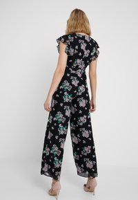Černý květinový overal s volánovými rukávy, širokými nohavicemi a přiléhavým tělem s růžovými a zelenými květinovými vzory.