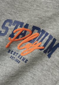 Il tessuto in cotone grigio presenta una scritta ricamata in blu navy e arancione che recita "STADIUM Gioca il Miglior Gioco" con una data di fondazione, finitura textured.