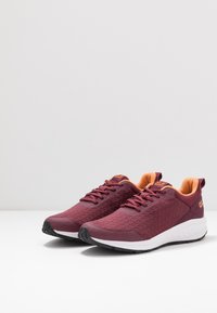 Maroon athletic sneakers with textured sides, orange interior lining, branded tongue and heel, white sole, and black outsole, angled right.