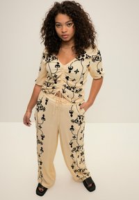 Completo beige a due pezzi con motivi floreali neri, top arricciato con scollatura a V e pantaloni larghi con vita regolabile.