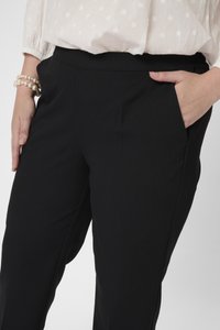 Schwarze, dehnbare Hosen mit einem elastischen Bund, Seitentaschen und einer glatten Textur. Kombiniert mit einem lässigen Oberteil und einem Perlenarmband.