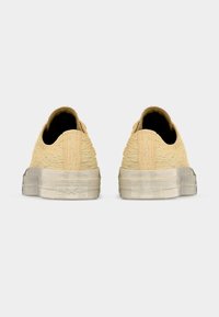 Baskets jaunes texturées avec un profil bas, une semelle en caoutchouc blanche lisse et sans lacets visibles, présentant un design simple.