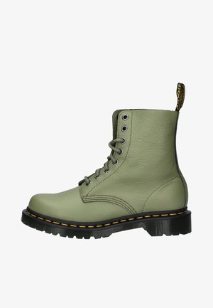 Grüne Lederkampfstiefel mit sechs Ösen, einer schwarzen Gummisohle, gelben Nähten und einem Ziehgriff auf der Rückseite. Strukturiertes Oberflächendesign.