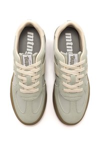 Par de zapatillas de ante verde claro y beige con cordones beige y suelas de goma marrón, vistas desde arriba sobre un fondo blanco.