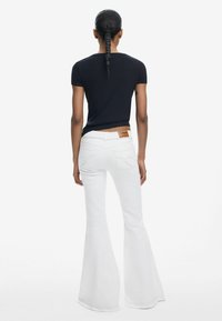 Witte flared jeans met een hoge taille, vijf zakken ontwerp en een tan leren merketiket; gecombineerd met een aansluitend zwart geribd t-shirt.