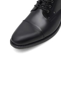 Czarne skórzane buty wizytowe z ostro zakończonym noskiem, charakteryzujące się gładką fakturą, wiązanym designem oraz kontrastowym szyciem wzdłuż cholewki.