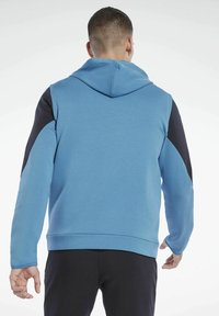 Felpa blu con cappuccio, con dettagli neri sulle spalle e maniche. Tessuto morbido, design aderente, polsini e orlo a costine.