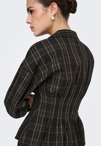 Veste peplum à carreaux noirs présentant une taille cintrée, des manches larges, et des lignes subtiles vertes et bordeaux, avec une texture tissée lisse.