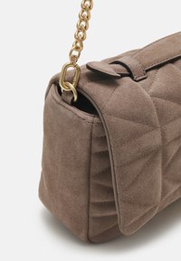 Borsa in camoscio marrone con un design trapuntato, una tracolla in catena dorata e una chiusura a pattina. La texture è morbida con una finitura opaca.