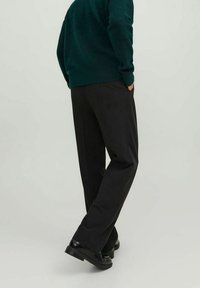 Svarta formella byxor med skräddarsydd passform, slät textur och en lätt lyster. Bärs tillsammans med en mörkgrön stickad tröja.