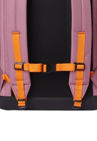 Primer plano de las correas de una mochila rosa con hebilla ajustable para el pecho de color naranja brillante y panel trasero de malla negra para ventilación.
