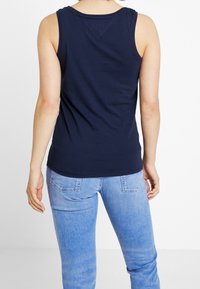 Granatowy top na ramiączkach o klasycznym prążkowanym wzorze. Miękka bawełniana tkanina, bez rękawów, z okrągłym dekoltem i nieco zaokrąglonym dołem. Połączony z jasnoniebieskimi dżinsami.