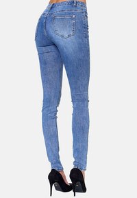Jeans ajustados de denim azul con una cintura de altura media, que presentan bolsillos traseros y una textura suave. Combinados con unos zapatos de tacón alto negros.