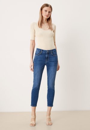 Top de canalé de color beige claro con mangas cortas, combinado con jeans ajustados de tiro medio en azul oscuro. Los jeans cuentan con un diseño clásico de cinco bolsillos.