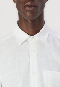 Camicia bianca in lino con colletto classico, patta con bottoni e taschino sul petto. Tessuto texturizzato con un aspetto leggero e traspirante.