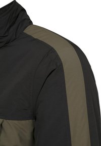 Svart jacka med olivgröna detaljer; texturerat tyg; hög krage; axeldetaljer med kontrasterande paneler.