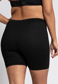Shorts neri elastici caratterizzati da una superficie liscia, lunghezza fino a metà coscia e una vita elasticizzata. Nessun motivo visibile o dettagli hardware.