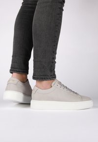 Sneaker grigie in suede con suola in gomma bianca, punta rotonda e design minimalista. I lacci e il branding sottile sul tallone accentuano lo stile.