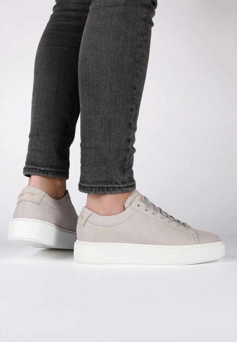 Sneaker grigie in suede con suola in gomma bianca, punta rotonda e design minimalista. I lacci e il branding sottile sul tallone accentuano lo stile.