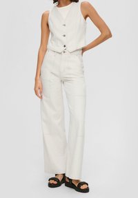 Weißer, kurzer Denim-Westen mit V-Ausschnitt und drei Knöpfen, kombiniert mit hoch taillierten, weit geschnittenen weißen Denim-Hosen mit sichtbaren Nähten.