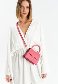 Borsetta in pelle rosa con un design strutturato, dotata di manico superiore e di una tracolla regolabile. Accenti in cuciture nere a contrasto.