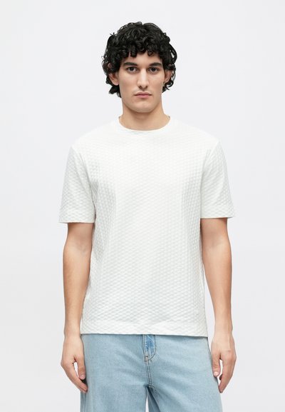 Άσπρο μπλουζάκι με υφή που διαθέτει διαμαντένιο μοτίβο, στρογγυλή λαιμόκοψη και κοντά μανίκια, συνδυασμένο με ανοιχτό μπλε τζιν σορτς.