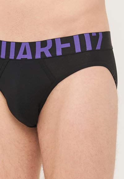 Mustat alushousut, joissa on purppuranvärinen elastinen vyötärö, jossa lukee suuret kirjaimet "MARF117". Sujuva kangas, perinteinen malli, kohtuullinen peittävyys.