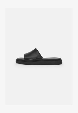 Sandal preto com uma parte superior em couro liso, uma faixa larga e uma sola plana em borracha, apresentando um design minimalista e sem ferragens visíveis.
