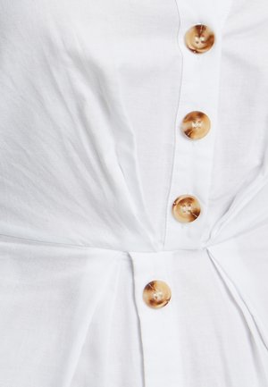 Valge linane särk, millel on kogutud vöökoht. Suured ümarad beežid nupud ja tekstureeritud kangas. Vertikaalne õmblusdetail lisab struktuuri.