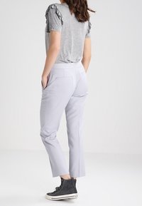 Gray t-shirt with ruffled sleeves, light gray fitted pants, and black high-top sneakers. Pants feature side pockets and a tailored fit.