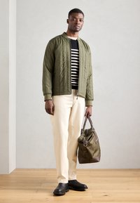 Giacca bomber trapuntata verde oliva, maglione a righe bianco e nero, pantaloni crema, zoccoli neri, borsa oliva con dettagli marroni.