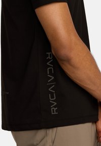 T-shirt nera a maniche corte in tessuto morbido, con stampa logo grigia sul lato e scollatura rotonda.