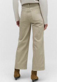 Beige vida byxor i en smidig tyg, med fem fickor och hög midja, kombinerat med bruna högklackade stövlar.