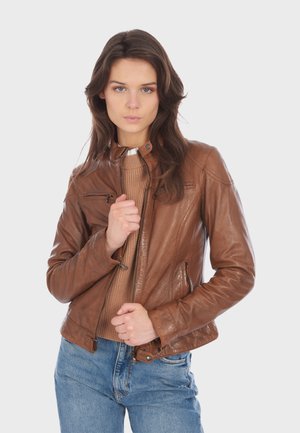 Brown leather jacket with a fitted cut, high collar, zippered pockets, and textured finish, paired with a ribbed sweater and jeans.