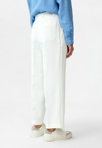 Witte, wijde broek met ribbeltextuur, met een achterzak en gefronste randen, gecombineerd met grijs-witte sneakers.