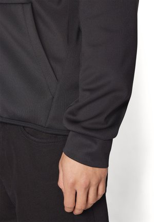Maglione sportivo nero realizzato in un tessuto testurizzato, con tasca a kangaroo e polsini a coste, abbinato a pantaloni scuri.