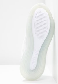 Semelle d'une basket blanche Nike Air Max avec bord extérieur translucide et bande de roulement texturée sur une surface blanche.