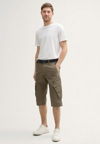 Lettet hvid bomulds-T-shirt, parret med mørke khaki cargo shorts med flere lommer og et sort bælte. Minimalistiske sneakers.
