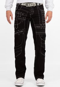 Jeans neri con cuciture bianche a contrasto, numerose tasche e dettagli borchiati. Abbinati a una cintura grigia e sneakers bianche.