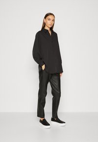 Black button-up shirt with long sleeves, paired with black leather pants and black slip-on sneakers with a white sole.