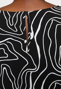 Černá látka s bílým abstraktním vzorem, s malým zapínáním na knoflík vzadu a s otvorem ve tvaru klíče pod výstřihem.