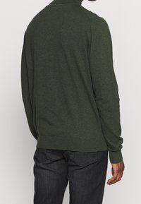 Pull en tricot vert foncé avec un col montant, des poignets côtelés et un ourlet ajusté. Texture lisse, design décontracté et manches longues.