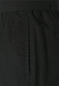 Černé kalhoty vyrobené z texturované tkaniny, mají pas a boční kapsu. Design zahrnuje sklady pro větší detail. Čistý a minimalistický design.