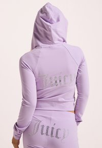 Lila, kurz geschnittenes Hoodie mit Kapuze, das auf der Rückseite mit Strassbuchstaben "Juicy" versehen ist. Hergestellt aus weichem, dehnbarem Material mit glatter Textur.