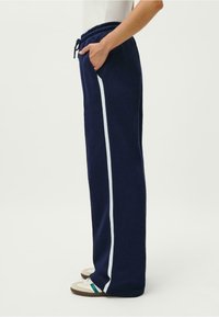 Jūras spēku sporta bikses ar brīvu piegriezumu, ar baltām sānu joslām, elastīgu jostu ar auklu un sānu kabatām.