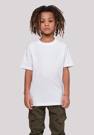 Child with medium brown dreadlocks wearing a plain white T-shirt and olive green cargo pants standing against a light gray background.