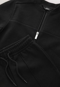 Conjunto de sudadera y pantalones deportivos negros. La sudadera presenta un cierre de cremallera y un tejido texturizado. Los pantalones deportivos tienen una cintura elástica con cordón ajustable.